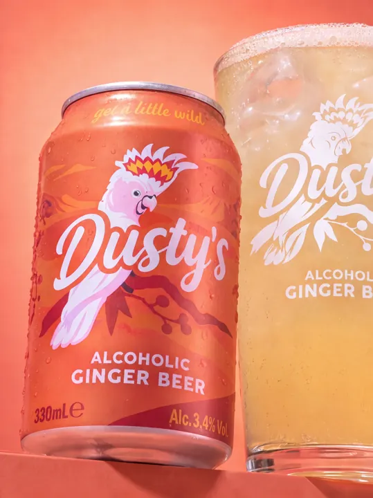 Low-angle view of a chilled Dusty's Ginger Beer can and branded pint glass