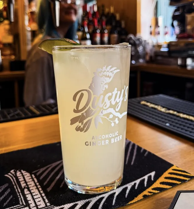Dusty's branded ginger beer pint glass with ice and lime on a pub bar