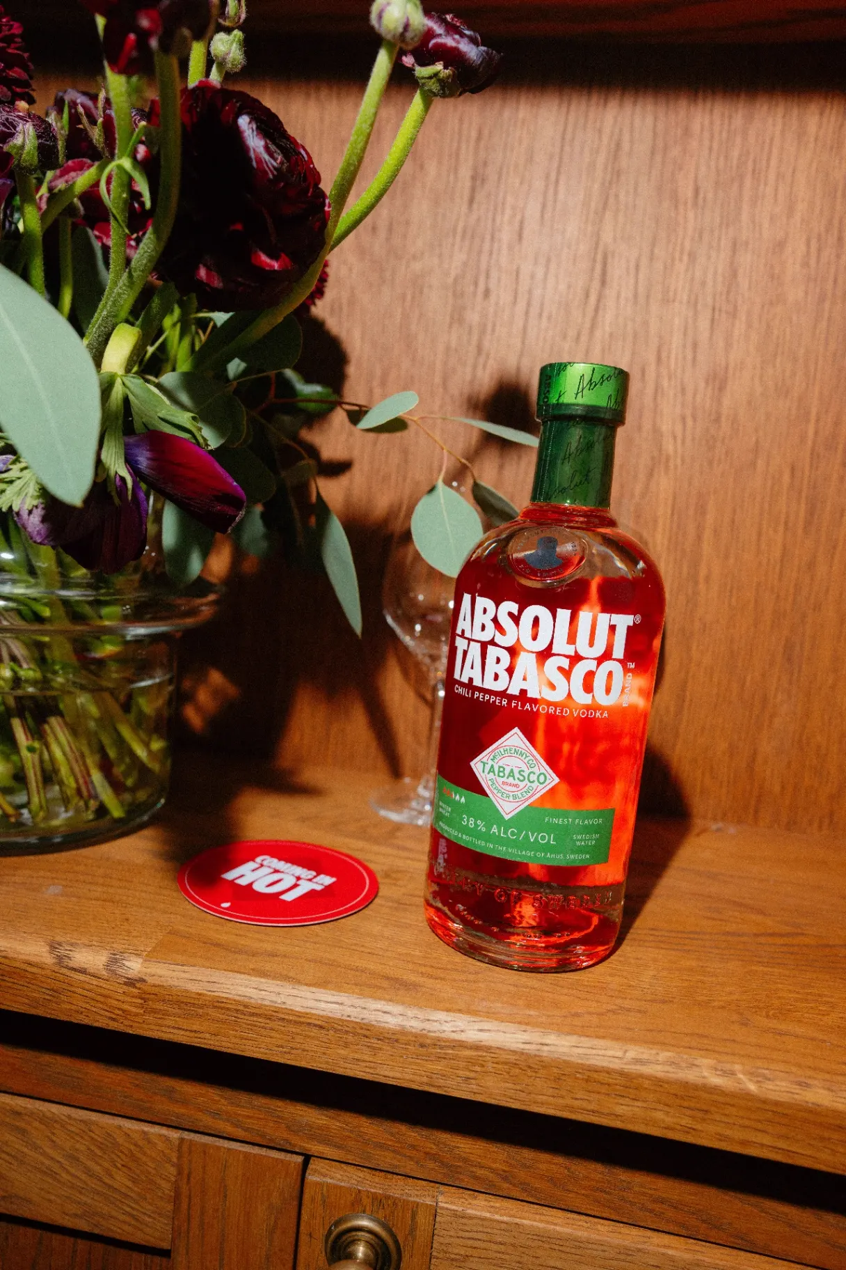 Absolut Tabasco bottle styled with dark red florals and a Coming In Hot coaster