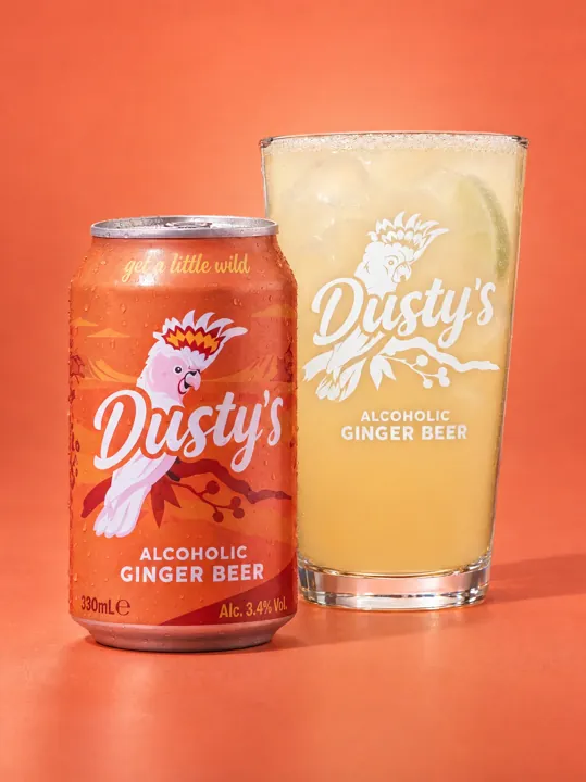 Dusty's Ginger Beer can beside a branded pint glass on a coral background