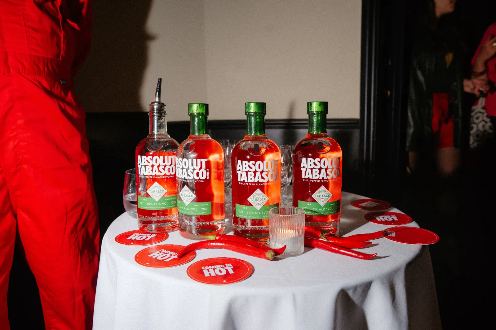 Four Absolut Tabasco bottles on a launch party table with red Coming In Hot coasters and chillies