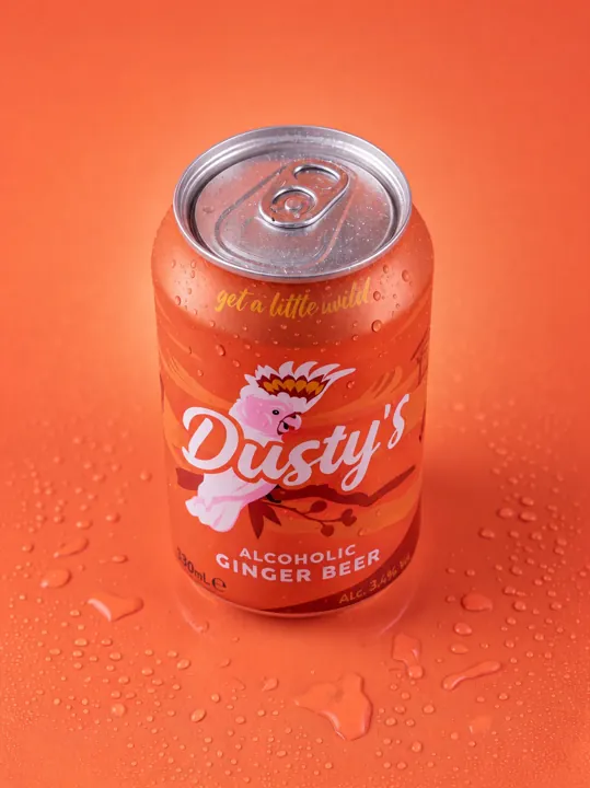 Top-angle view of a chilled Dusty's Ginger Beer can with water droplets on a coral surface